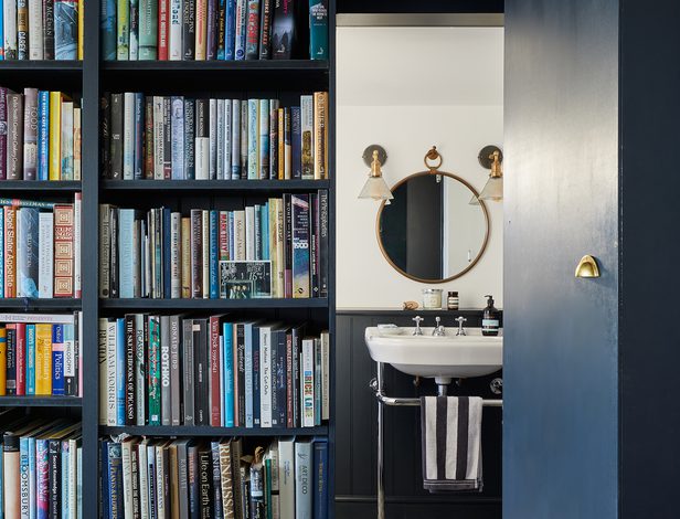 Inviting reading nook at Curlews, West Sussex, boasting a full bookshelf wall, cosy seating, and coastal-inspired accents.